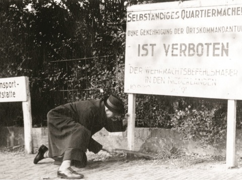 Keurig geklede Utrechtse man zaagt een bord van de Duitse Weermacht om